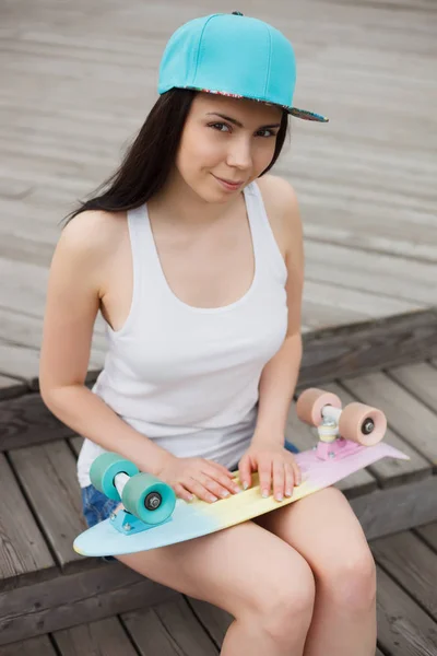 年轻的白色黑发女孩坐在户外与短巡洋舰滑板在夏日 流行的小滑板甲板 时尚的服装 漂亮的模型 — 图库照片