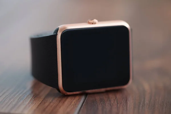 Modern smart watch on wooden background. Trendy new technology that let you always stay connected to internet and social media. Place text or app icon on blank black screen. Macro close up