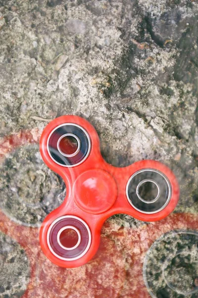 Red spinner fidget toy.Enjoy playing with modern spinning toys.Improve reaction & learn cool new balance tricks.Close up,old grungy stone background
