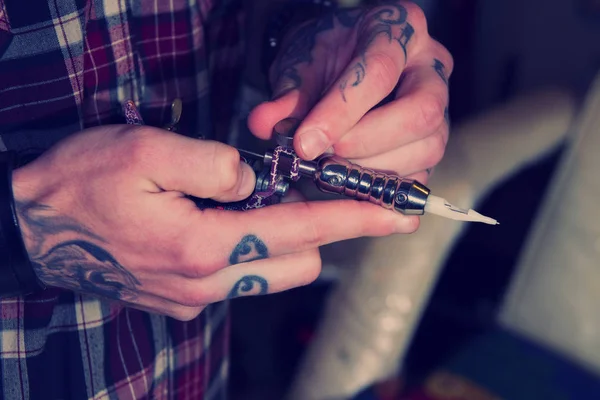 Master holding a machine for tattoo making. Heavy inked fingers, focus on a needle