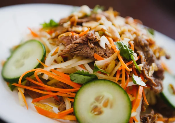 Eat tasty Chinese salad with beef meat,fresh cucumber & Asian carrot with melted nuts topping.Try exotic snack in Vietnam restaurant with traditional food.Close up,focus on salad.