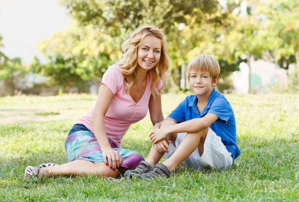 迷人的金发女青年和小男孩坐在绿色的公园里 快乐的母亲和儿子 — 图库照片