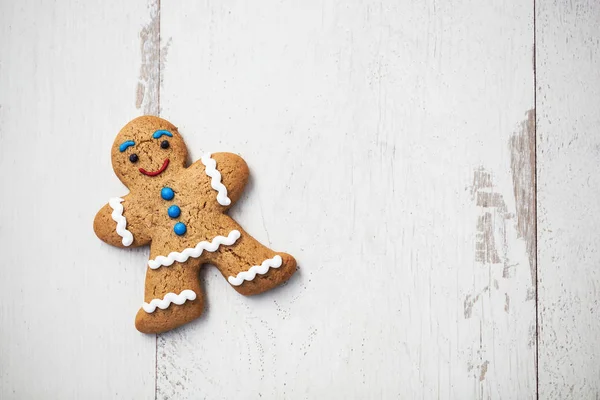 Gingerbread cookie in shape of person lying on wooden table. Smiling eatable character with good taste. Close up macro, copy space on bright white wood