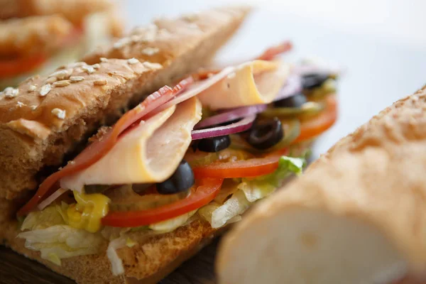 Fresh sandwiches with tomato,ham & parmesan cheese slice,black olives & mustard sauce on table in cafe. Fast food restaurant menu close up. Delicious street food dish.