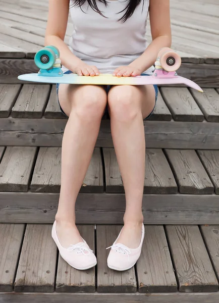 屋外夏の日で短い巡洋艦のスケート ボードを持って座っている若い女性 人気の小さなスケート デッキ 流行の服 認識できないモデルの足に焦点を当てる — ストック写真