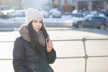 Güzel beyaz esmer kız vaping parlak soğuk kış günü açık. Çekici kadın modeli ile sigara eliquid veya e-suyu için popüler electrnoic becerikli alet. Vape ejuice için atomizer mod 