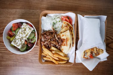 Üstten görünüm fotoğraf traiditional Yunan fast food menü kızarmış et souvlaki ve kavrulmuş gyros çanak ile. Sağlıklı taze Yunan salatası kağıt tabak içinde servis. Fast food restoran götürün