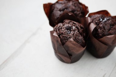 Beyaz ahşap masa üzerinde üç taze çikolatalı kek. Ev yapımı ekmek, kahve molası için almak muffin. Odak kadar yakın, metin eklemek için alanı Kopyala