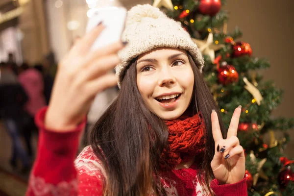 年轻女子采取自拍与智能手机 并显示胜利手势 — 图库照片