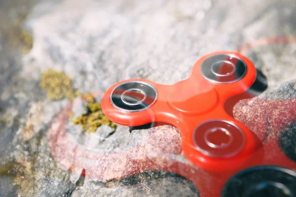 Red spinner fidget toy.Enjoy playing with modern spinning toys.Improve reaction & learn cool new balance tricks.Old grungy stone background,focus on device