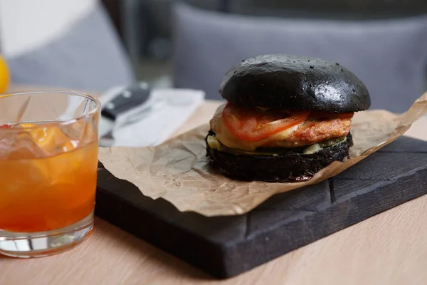 Enjoy big black burger with beef meat cutlet in cursty bun served with fresh tomato slice & burned cheese on wooden plate in fast food cafe menu.Meat restaurant menu item