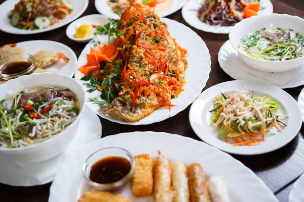 Closeup shot of spicy fried karp fish with traditional Vietnamese salads & seafood.Big Asian restaurant dinner in macro.Shrimp roll,eel salad & pho bo soup served on table in China cafe