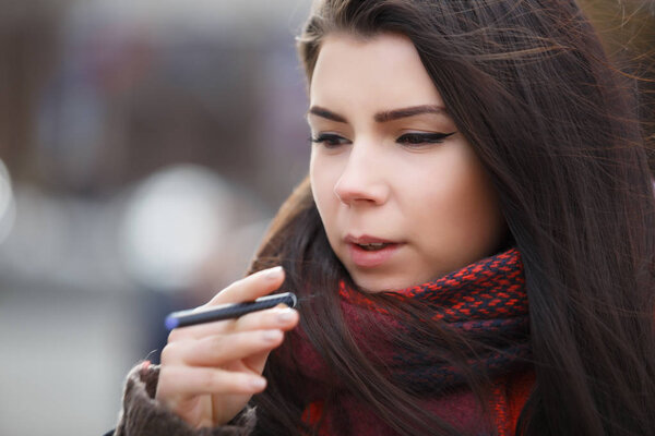 Грустная молодая брюнетка девушка курение электронных сигарет или ecig gadget.Modern vaping устройство палку бросить курить nicotine.Young курильщик женщина курить небольшие черные электронные сигареты ручку outdoor.Bad злоупотребление здоровьем habbit
