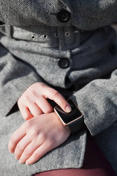 Female using her trendy smart wrist watch sitting on the bench. This person is always connected to social media and internet.