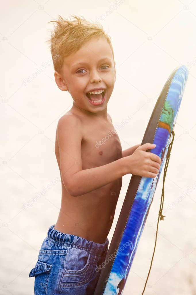 Funny little boy with blue surfing board on the beach