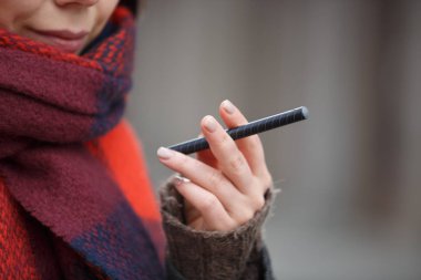 Küçük siyah elektronik vape kalem ecig aygıtı üzerinde odaklanın. Genç gülümseyen kadın sigara içen e-cig gadet ile el. Sigara nikotin çıkın, vaping e-suyu başlar. Sigara içen kötü alışkanlıktan, sağlık kötüye. Sağlıksız yaşam tarzı