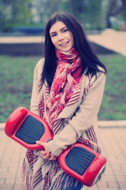 Esmer beyaz girll modern kırmızı elektrikli mini segway ya da vurgulu kurulu scooter parkta yürürken elinde tutan. Popüler yeni becerikli alet. Kız trendy boho tarzı kıyafetler giyiyor.