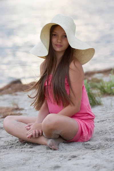 可爱的年轻女孩在帽子坐在沙滩上 — 图库照片