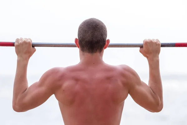 Handsome young man doing street workout on the beach in a bright summer day.