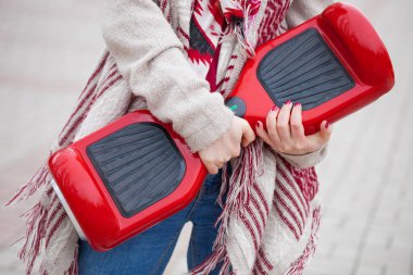 Modern kırmızı elektrikli mini segway ya da vurgulu kurulu scooter parkta yürürken elinde tutan Womanl. Hava kirliliği atmosfere üreten popüler yeni ulaşım teknolojisi. Kız gidişli boho tarzı kıyafetler giyiyor.