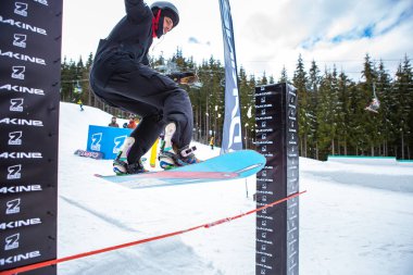 Bukovel, Ukrayna-19 Mart, 2018: Snowboarder çubuğunun üzerine atlar sıcak kış spor giyim ve kar kurulu güvertede ayak Bukovel kış Park.Fun etkinliğinde aktif genç atletler için