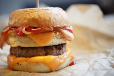 Lezzetli, büyük, çift katlı hamburger. Amerikan fast food restoranı menüsü. Soslu ızgara büyük hamburger, kahverengi kağıtta servis edilen domuz peyniri.