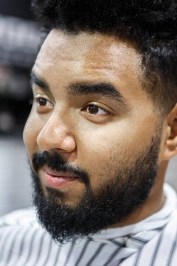 Yakışıklı genç siyah adamla tıraşsız sakal ve bıyık Berber Kuaför Kuaför için onun saç kesmek bekleyen içinde döşeme bıyık ve sakal. Erkek güzellik tedavi kavramı. Kuaför müşteri portre