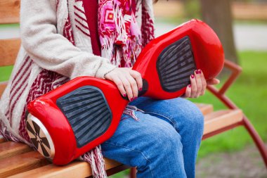 Boho stil elbiseleri modern elektrikli mini segway veya vurgulu kurulu scooter elinde tutan bir bankta oturan kız. Hava kirliliği atmosfere üreten yeni ulaşım teknolojisi eğilimleri. Tanınmayan model ve devic üzerinde Kapat