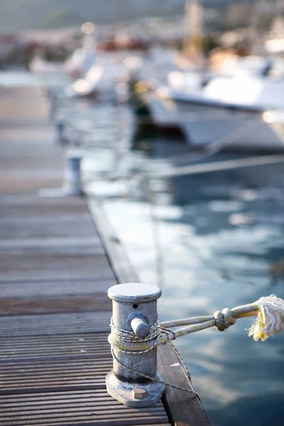 Mooring bollard on pier in harbor.Water craft tied to shore with knot.Popular travel destination.Rent a boat for summer vacation trip.Vertical shot, focus on steel floating construction in haven