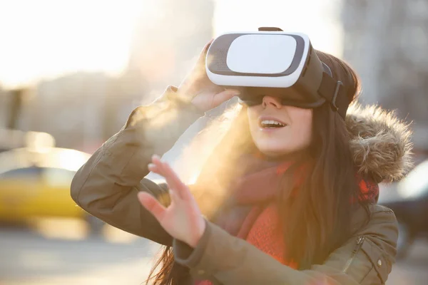 Young female play with super cool virtual reality glasses for mobile gaming applications outdoor in sunset.Use mobile apps with innovative vr headset.Trendy augmented reality gamer gadget in use