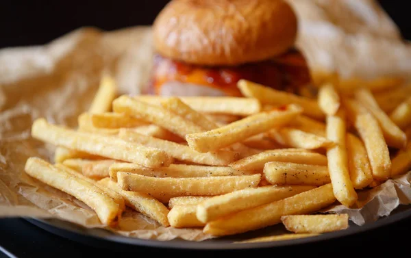 Delicious big fat crafted hamburger served on brown decorative paper in fast food restaurant menu.Tasty,but unhealthy junk food with fat meat,sauce & French fries on plate in cafe