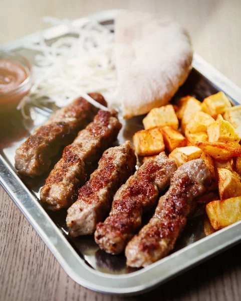 Traditional Serbian roasted meat dish served with fried potato.Exotic grilled beef in fast food restaurant menu.Fat smoked dish background close up.