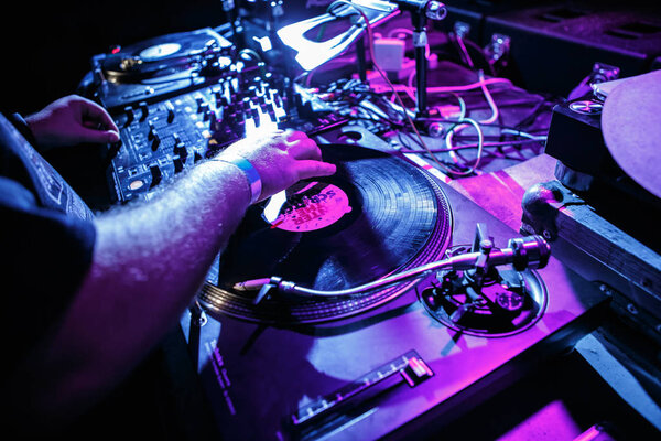 KIEV-4 JULY,2018: Dj Panchez scratches vinyl records on retro Technics turntable player device in night club on party.Overhead view of turn tables at concert stage in blue and magenta lights