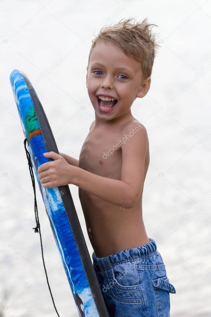 Funny little boy with blue surfing board on the beach