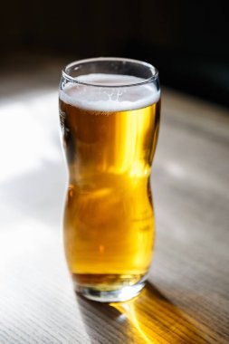 Işık lager bira ile parlak cam. Düşük köpük balonlar ve güneşin altın sıvı Parlatıcı. Kristal berraklığında bira cam güneş ışığı bir barda masada. Dikey yakından atış