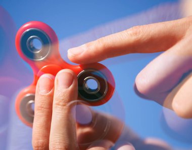 Serin yeni topluca spinner oyuncak. Kadın oyun modern iplik cihazı ile. Rulman ortada dönen süper trendy bu becerikli alet ile oynarken zevk. Parlak mavi gökyüzü arka plan
