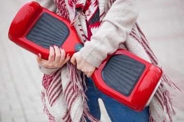 Modern kırmızı elektrikli mini segway ya da vurgulu kurulu scooter parkta yürürken elinde tutan Womanl. Hava kirliliği atmosfere üreten popüler yeni ulaşım teknolojisi. Kız gidişli boho tarzı kıyafetler giyiyor.