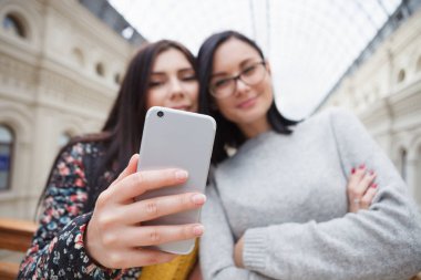 İki genç kız selfie portre fotoğraf alışveriş merkezinde çekici kamera ile akıllı telefon odaklan. İyi bir lens ile büyük gümüş smartphone. Harika fotoğraf çekmek