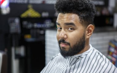 Yakışıklı genç siyah adam portresi berber salonu battaniyeye kaplı. İstemci Kuaför Kuaför onu yeni saç kesimi, saç sakal ve bıyık aşağı kesim yapmak için bekliyor. Erkek güzellik bakımı