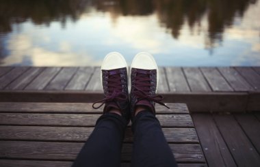 Yenilikçi bir bankta oturan moda marsala spor ayakkabı giyen kadın metrelik. Nehir ya da göl arka plan '. Sakin ve huzurlu ruh hali.