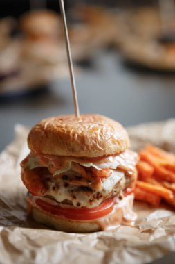 Dikey yakın kadar huysuz topuz taze burgeri vuruşta. Hamburger kuzu eti ve yanık peynir dilimi ile fastfood Cafe kahverengi kağıt tabakta servis. Abur cubur restoran menü, kötü Diyet