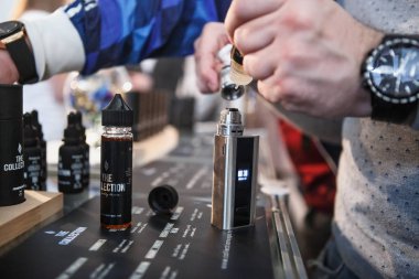 KIEV, UKRAINE - 14 APRIL, 2018: Specialist fill mech mod vaping devices with e-liquid on sale at Vape Expo event.Buy new electronic cigarette vaporizer for smoking ejuice liquid.Ecig gadget for smokers clipart