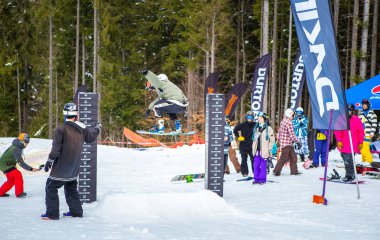 Bukovel, Ukrayna-19 Mart, 2018: Snowboarder çubuğunun üzerine atlar sıcak kış spor giyim ve kar kurulu güvertede ayak Bukovel kış Park.Fun etkinliğinde aktif genç atletler için