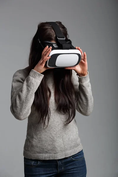 Studio portrait of young brunette girl playing with virtual reality goggles for mobile game application.Girl use mobile games apps with innovative 3d vr headset.Trendy augmented reality gadget in use