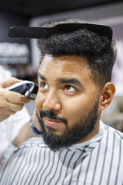 Портрет красивого черного парня с расческой в прическе. Парикмахерская для стрижки клиентской бороды с помощью станка стрижки.
