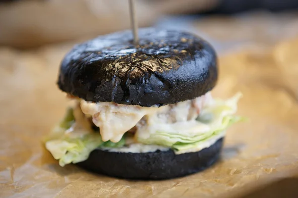 Big tasty black burger in fast food restaurant menu .Delicious sauce & green lettuce salad leaves in crusty bun. Grilled beef meat peace.Fat junk food in American cafe menu