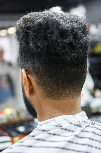 Young black man in barber shop covered with blanket waiting for barber hairdresser to trim his neck and make pretty haircut.Male beauty treatment process in close up