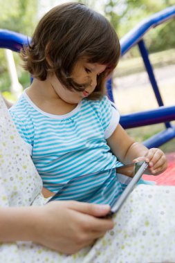 İki kardeş yeşil parkta bir bankta trendy tablet pc ile oynama