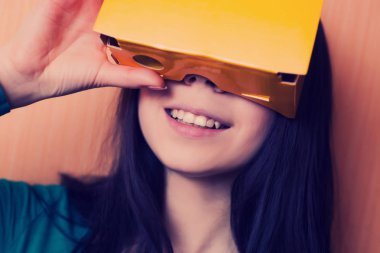 Genç kız eğlenmek onu karton vr mezartaşı ile oynarken onun akıllı telefona bağlı. Hipster renk ve modern teknoloji