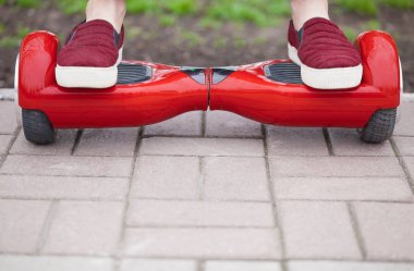 Bir kız bir modern kırmızı elektrikli mini segway ya da vurgulu yönetim kurulu üzerinde sürme marsala ayakkabı ayakları üzerinde Cllose kadar. Çok eğlenceli ve basit-e doğru binmek ve hava kirliliği atmosfere üreten yeni ulaşım teknolojisinin eğilimleri.